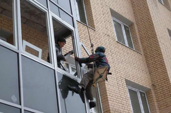 Промышленный альпинист выполняет фасадное остекление балкона